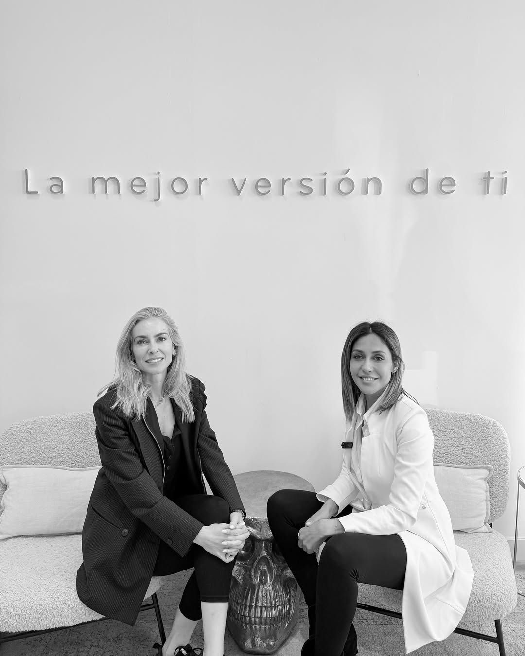 Dos mujeres están sentadas en un sofá frente a un cartel que dice la mejor versión de ti.