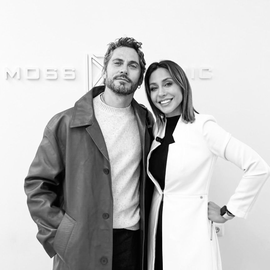Un hombre y una mujer posan para una foto frente a un cartel de música de Moss.