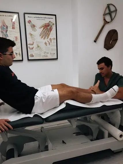 Un hombre con una pierna escayolada recibe atención médica en una consulta. Hay carteles colgados en la pared.