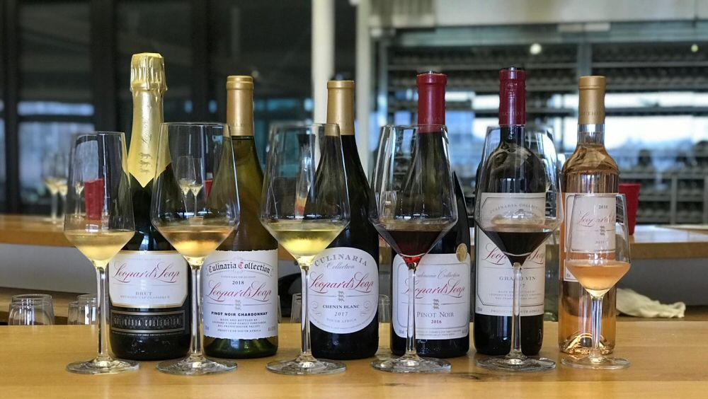 Wine bottles and glasses on a wooden counter, showcasing various colors of wine in a restaurant setting.