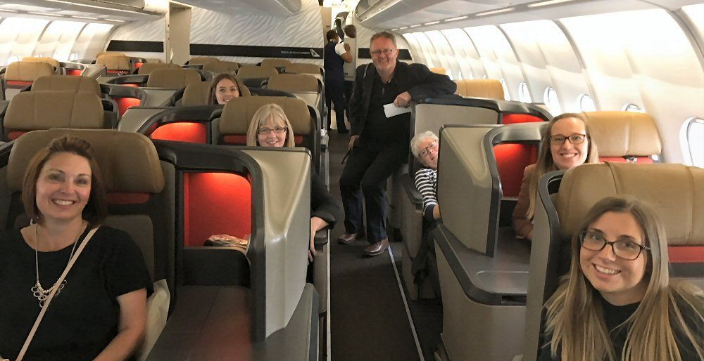 People smiling in airplane cabin with brown and gray seats.