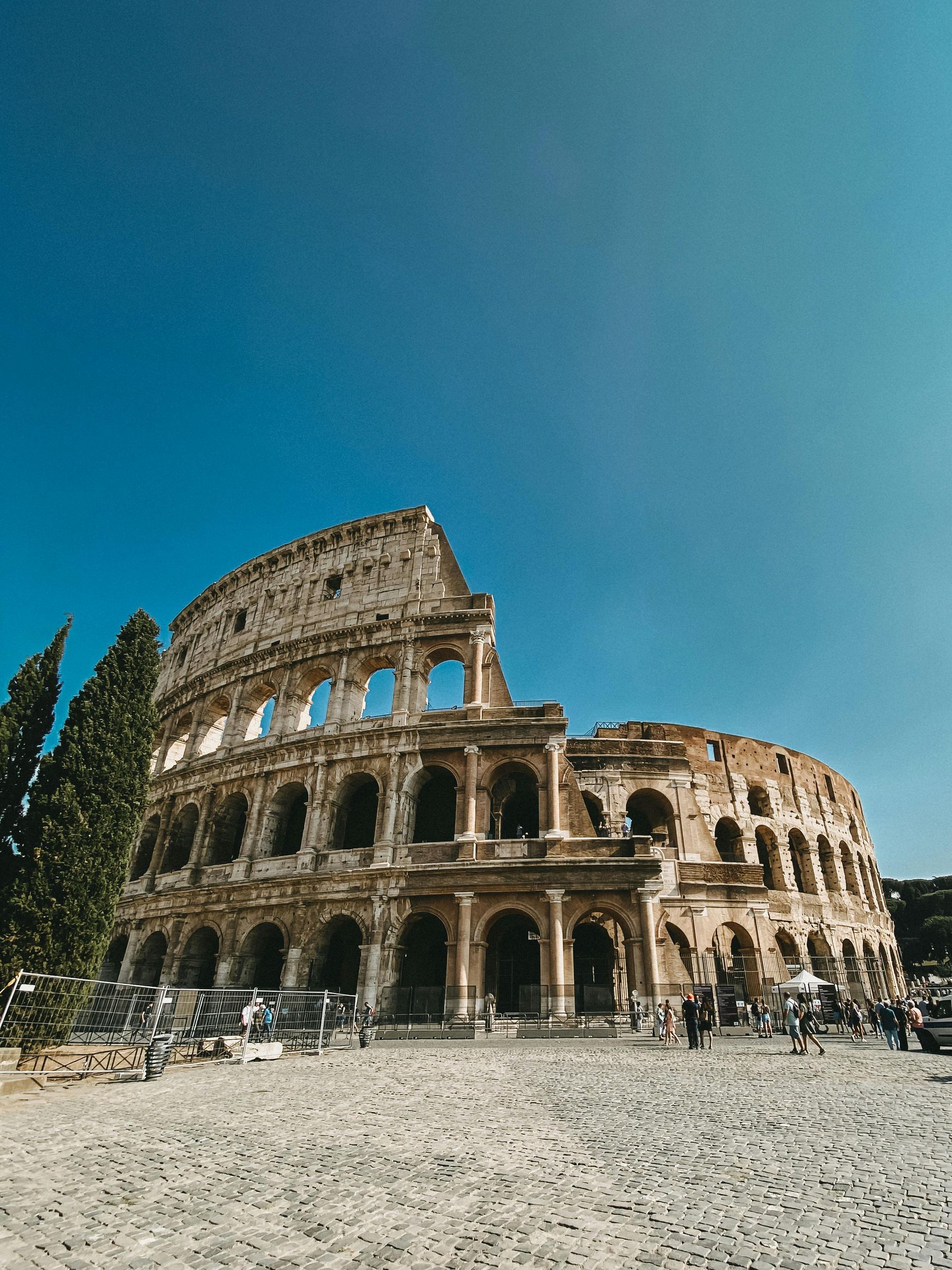 Colosseum in Rome, Italy. Ancient amphitheater with arched openings, partially ruined. Blue sky, tourists.