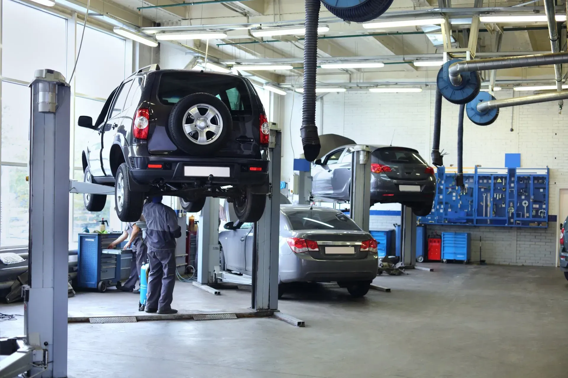 Atelier de réparation automobile avec deux voitures sur des ponts élévateurs et un mécanicien travaillant