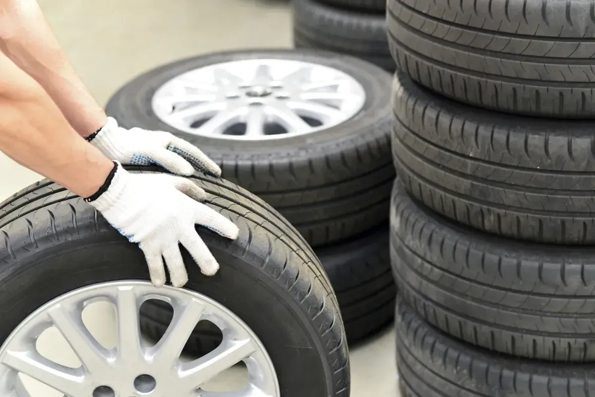Des mains gantées de blanc inspectent un pneu de voiture à côté de pneus