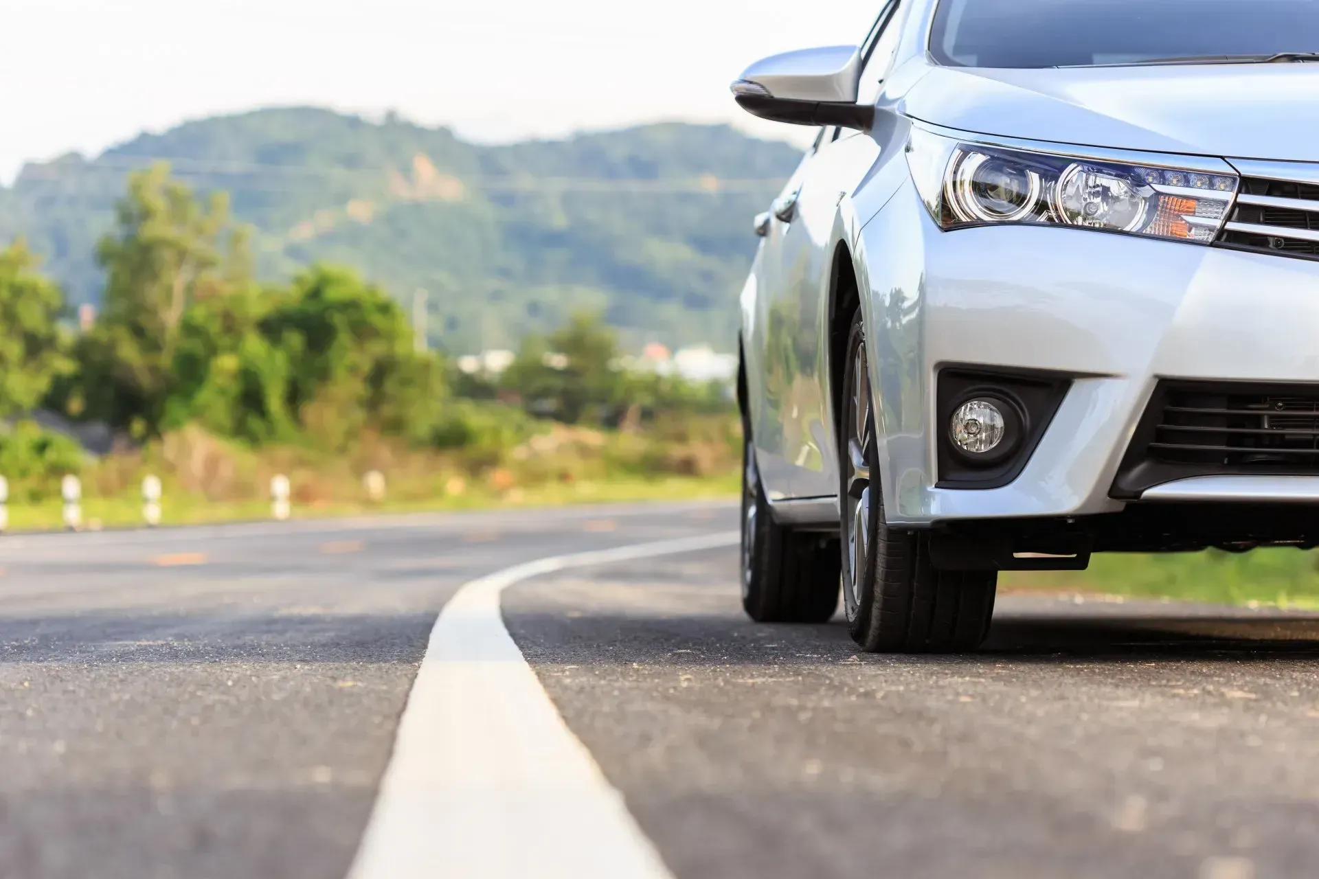Voiture argentée roulant sur une route sinueuse avec des collines floues