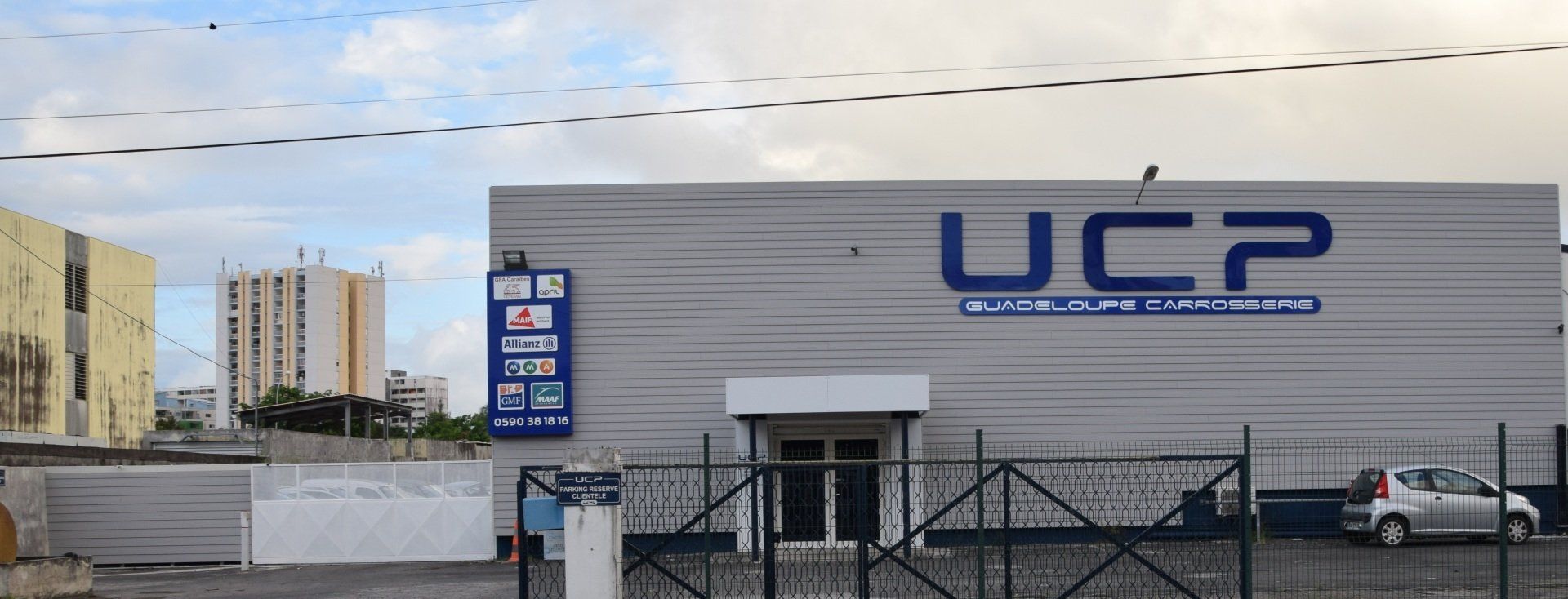 La devanture grise de UCP Guadeloupe Carrosserie avec un panneau à côté.
