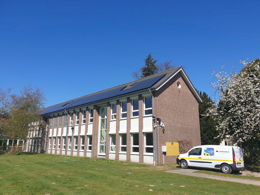 Ein weißer Lieferwagen parkt vor einem Gebäude mit Solarzellen auf dem Dach.
