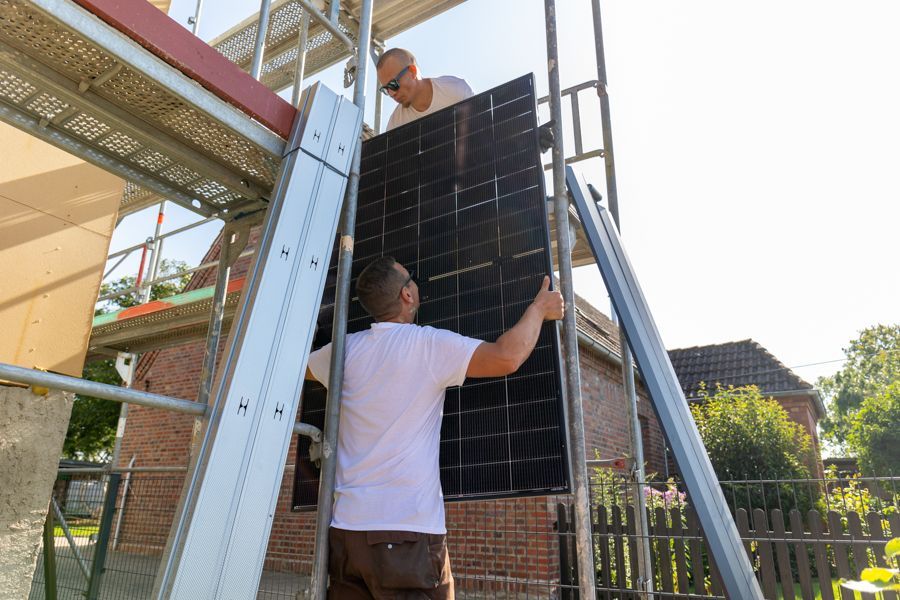 Zwei Männer installieren auf einem Gerüst ein Solarpanel.