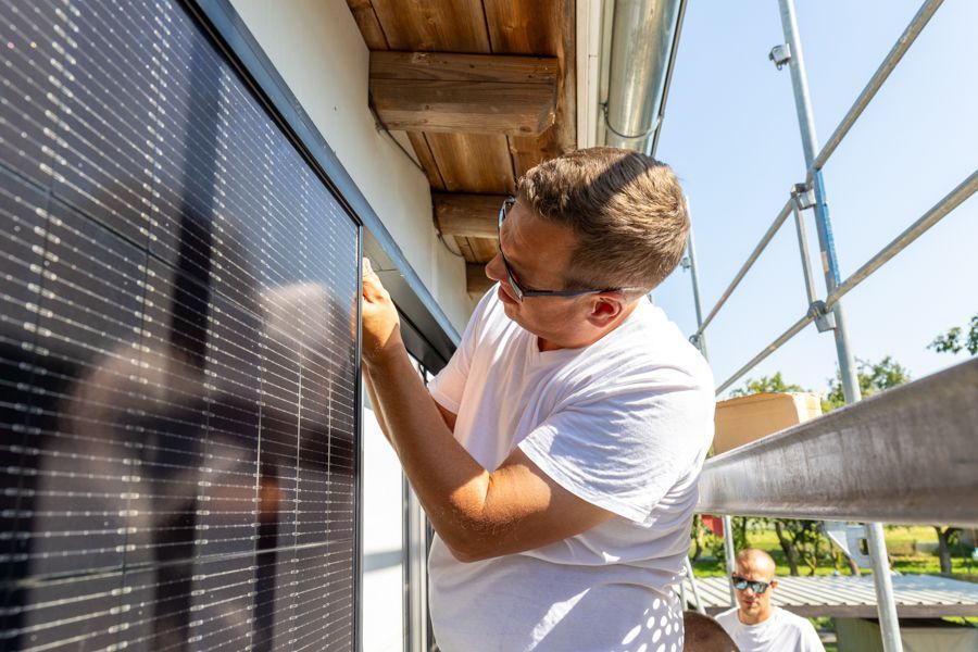 Ein Mann installiert ein Solarpanel an der Seite eines Gebäudes.