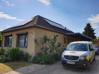 Ein weißer Lieferwagen parkt vor einem Backsteinhaus mit Solarzellen auf dem Dach.