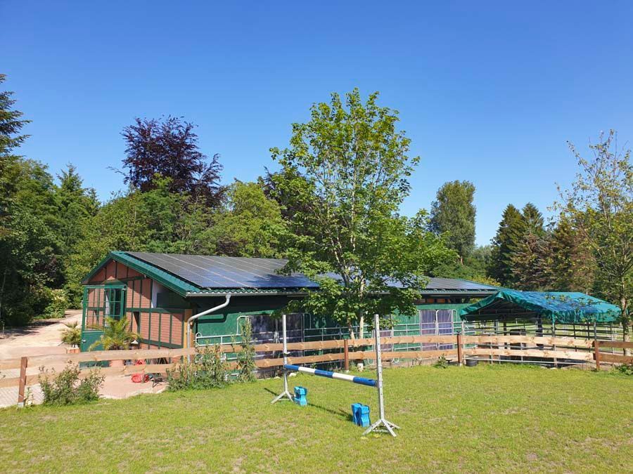 Ein Gewächshaus mit Sonnenkollektoren auf dem Dach ist von Bäumen und Gras umgeben.