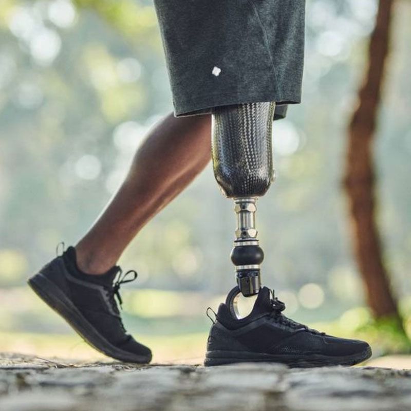 Persona caminando al aire libre, con una pierna protésica y zapatillas deportivas negras.