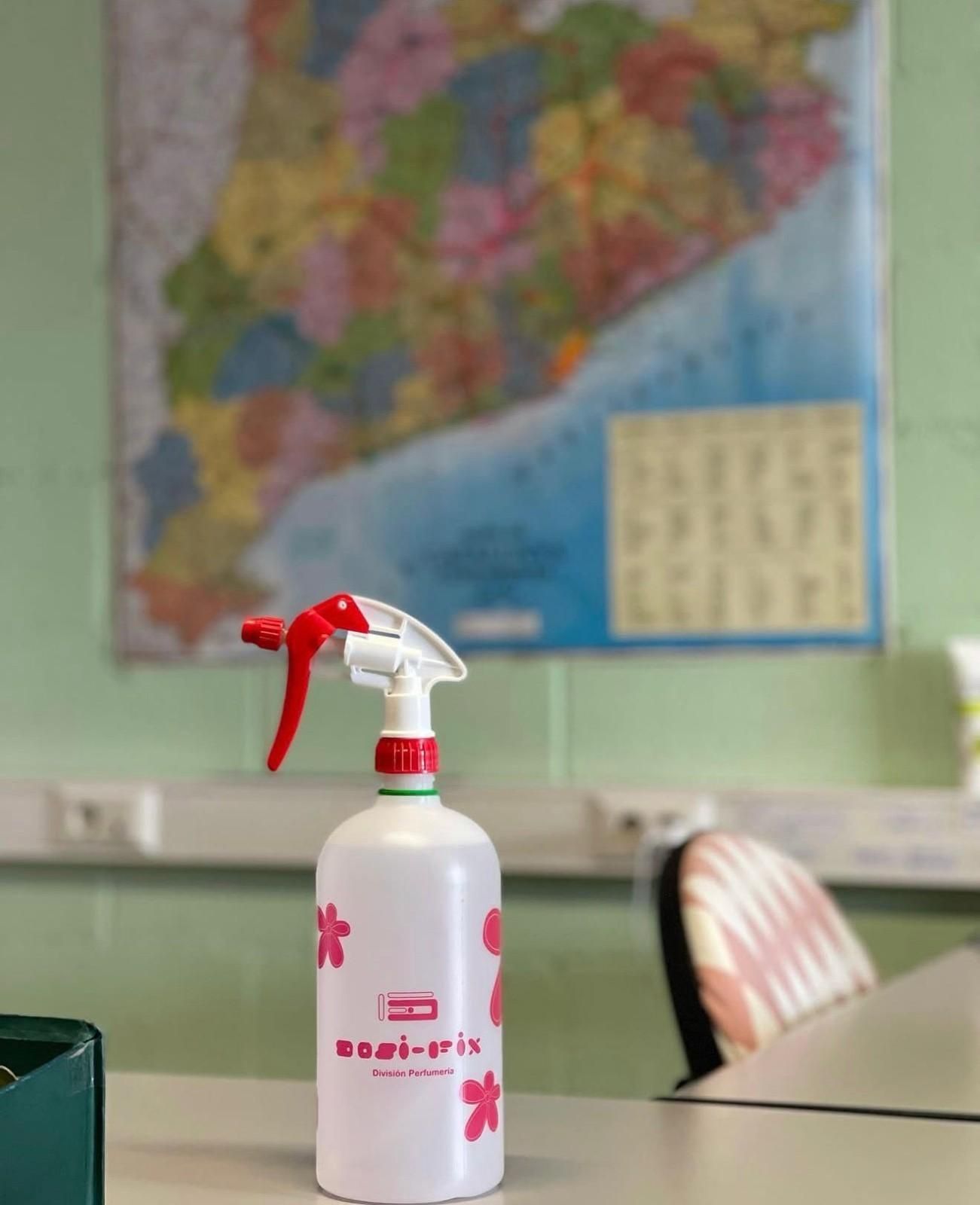 Un frasco de spray rosa sobre un escritorio en un aula, con un mapa colorido en la pared detrás.