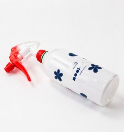 Botella pulverizadora blanca con estampado floral azul y boquilla roja sobre una superficie blanca.