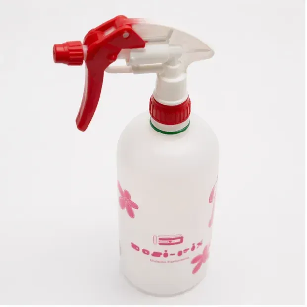 Botella pulverizadora blanca con boquilla de gatillo roja y diseño floral rosa sobre fondo liso.