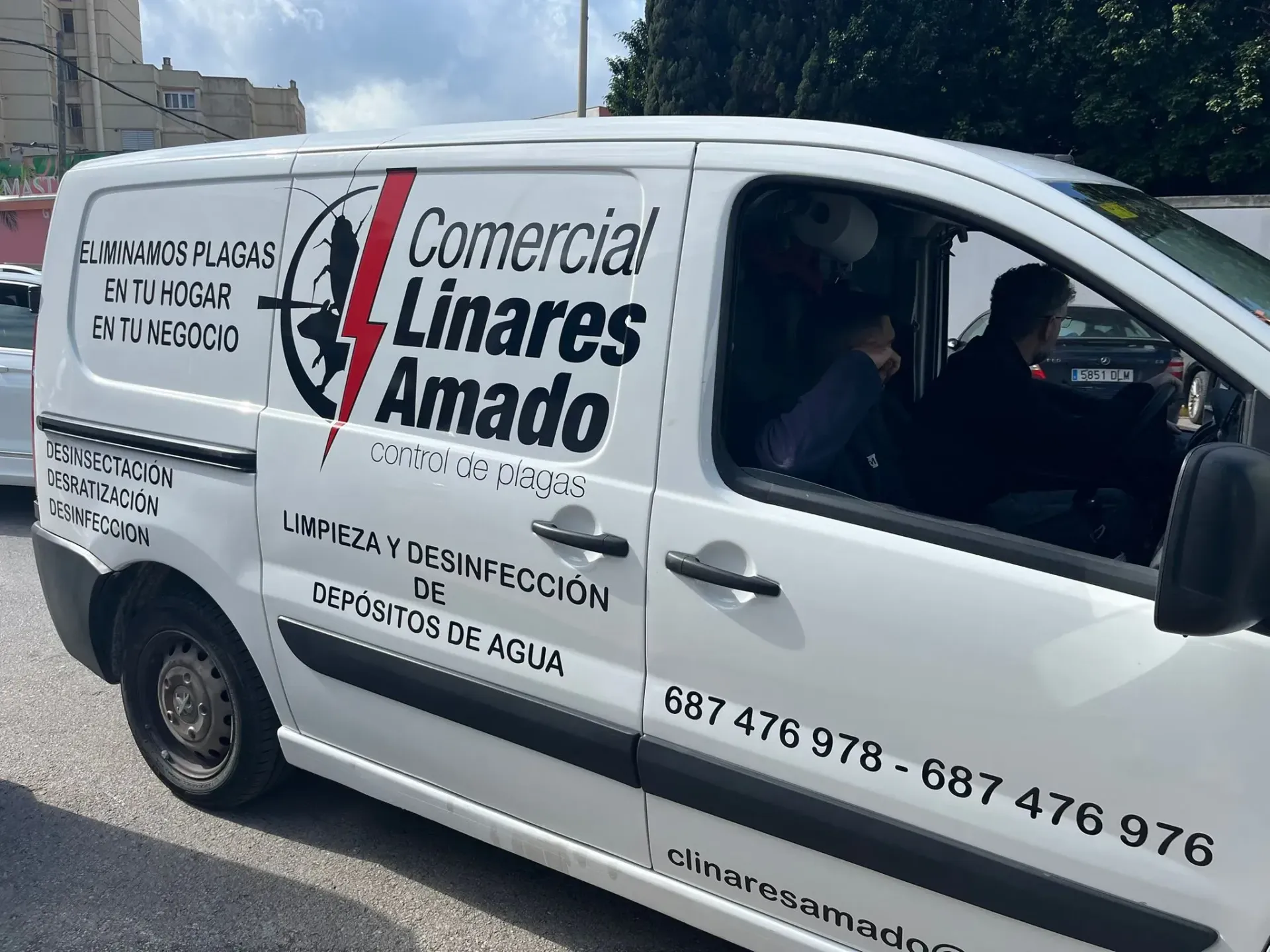 Tres trabajadores con trajes protectores amarillos y mascarillas limpian las ventanas de un edificio de ladrillo.