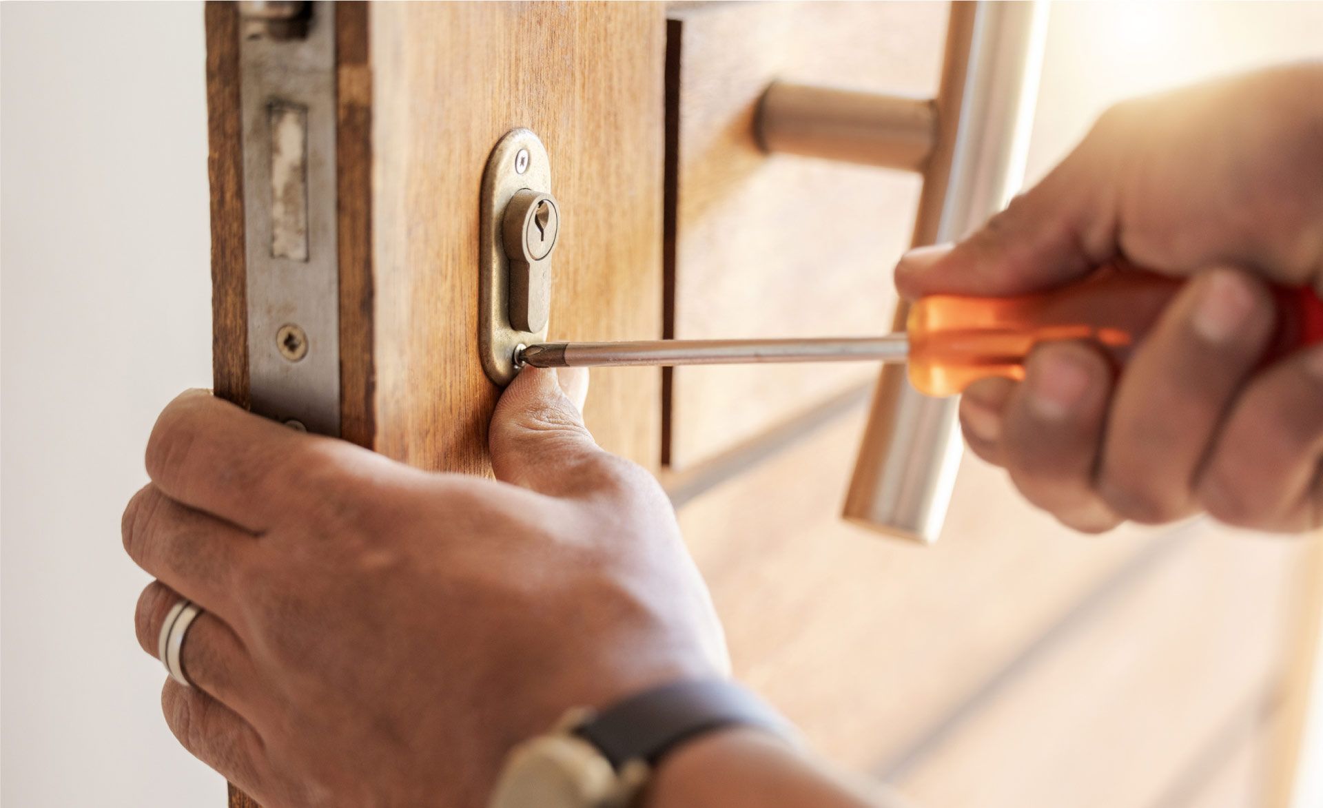 Persona usando un destornillador para arreglar la cerradura de una puerta. El primer plano muestra las manos, la puerta de madera y un destornillador naranja.