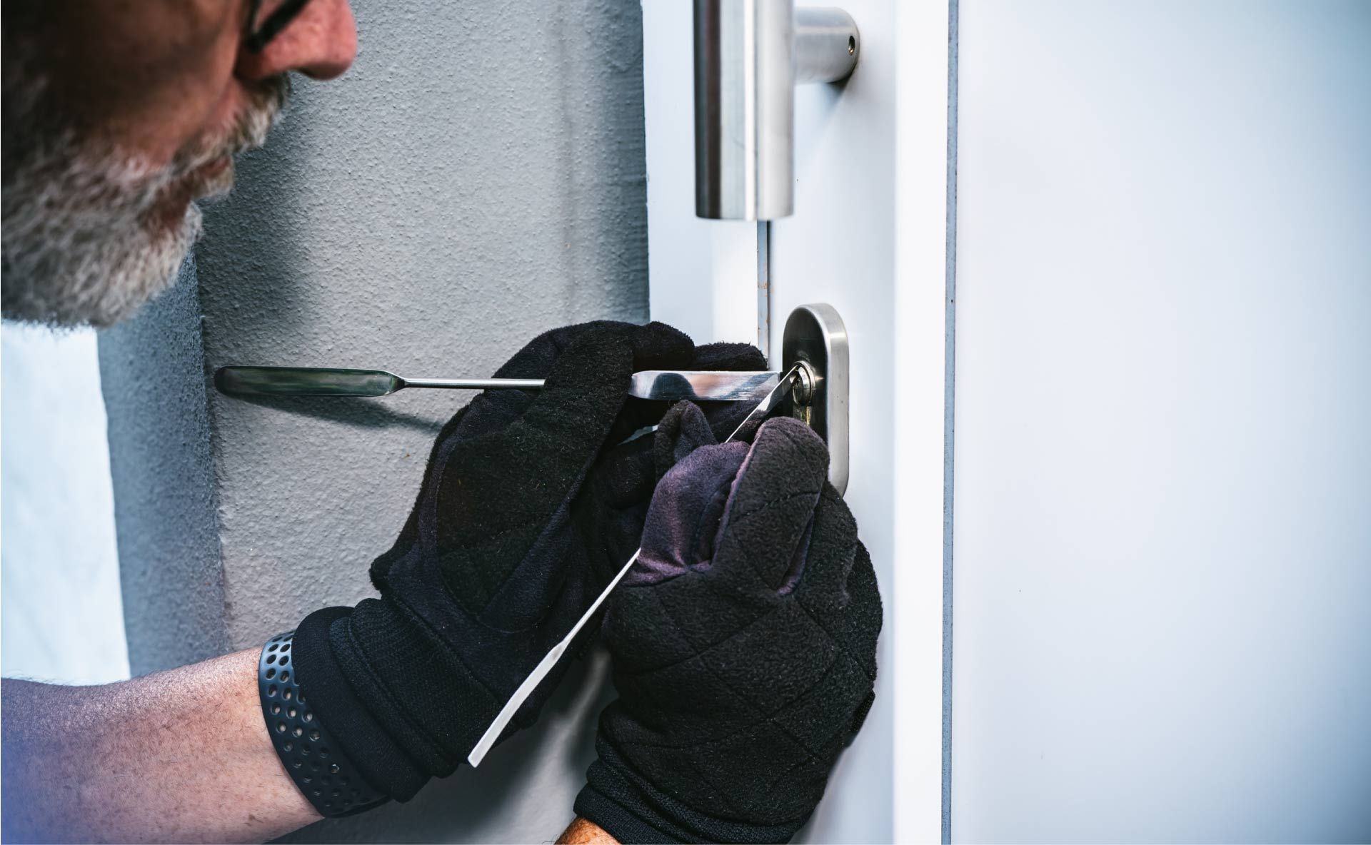 Persona que lleva guantes negros abriendo una cerradura de puerta con herramientas; primer plano.