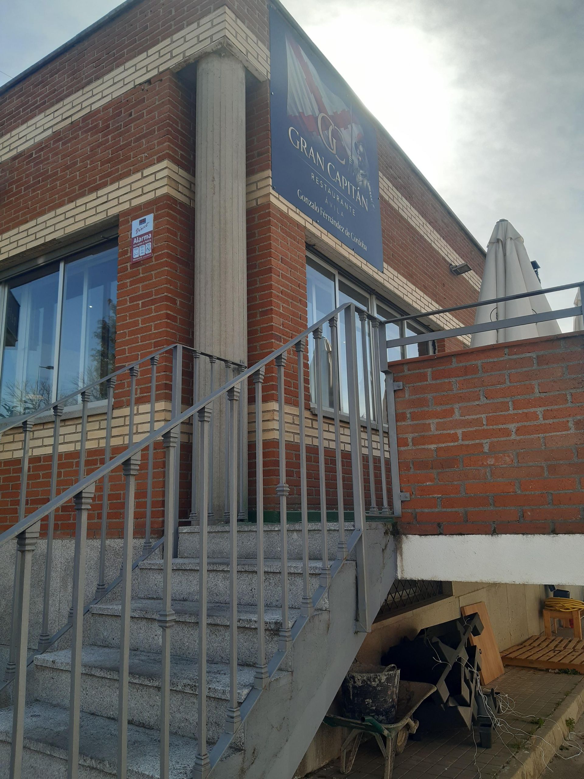 Vista desde un ángulo bajo de un edificio de ladrillo con una escalera de piedra y una barandilla de metal que conduce a una entrada lateral.