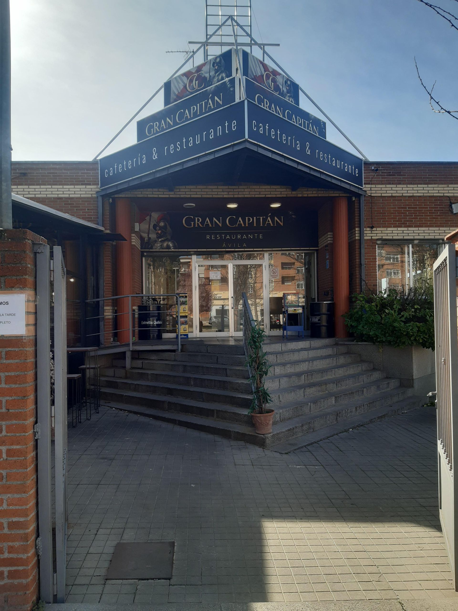 Una entrada de ladrillo con un toldo triangular, escaleras de piedra y puertas de cristal con la inscripción 