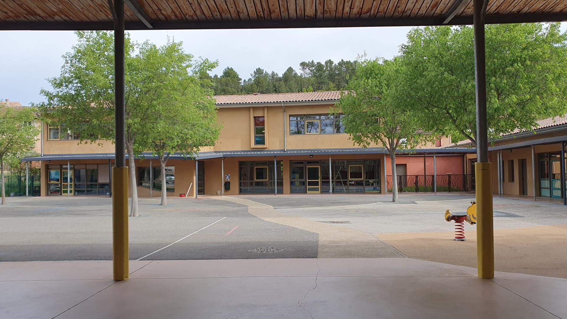 Cour d'école avec bâtiments et arbres vue depuis une allée couverte.