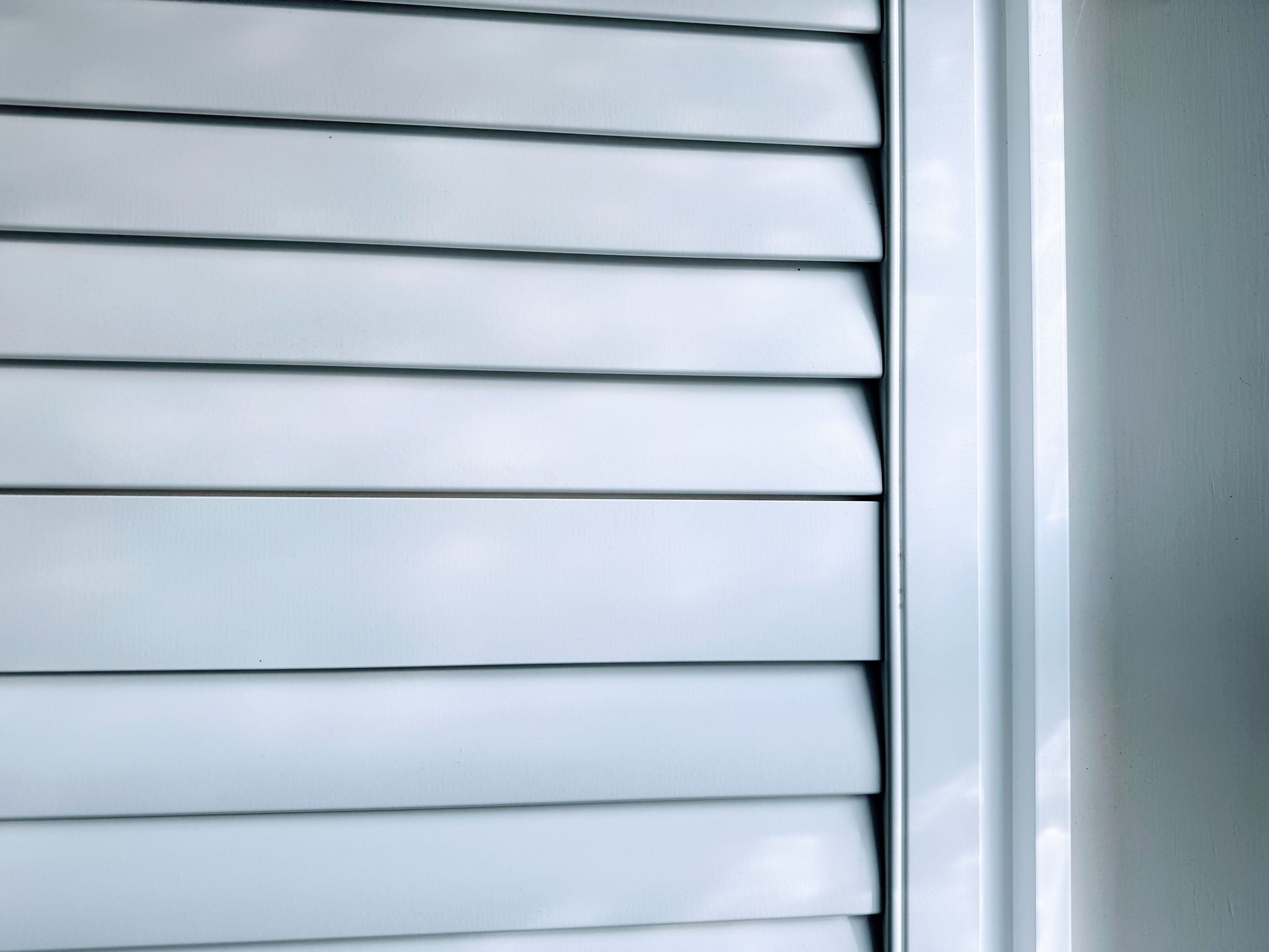 Volets persiennes blancs, partiellement ouverts, sur un cadre et un mur blancs.