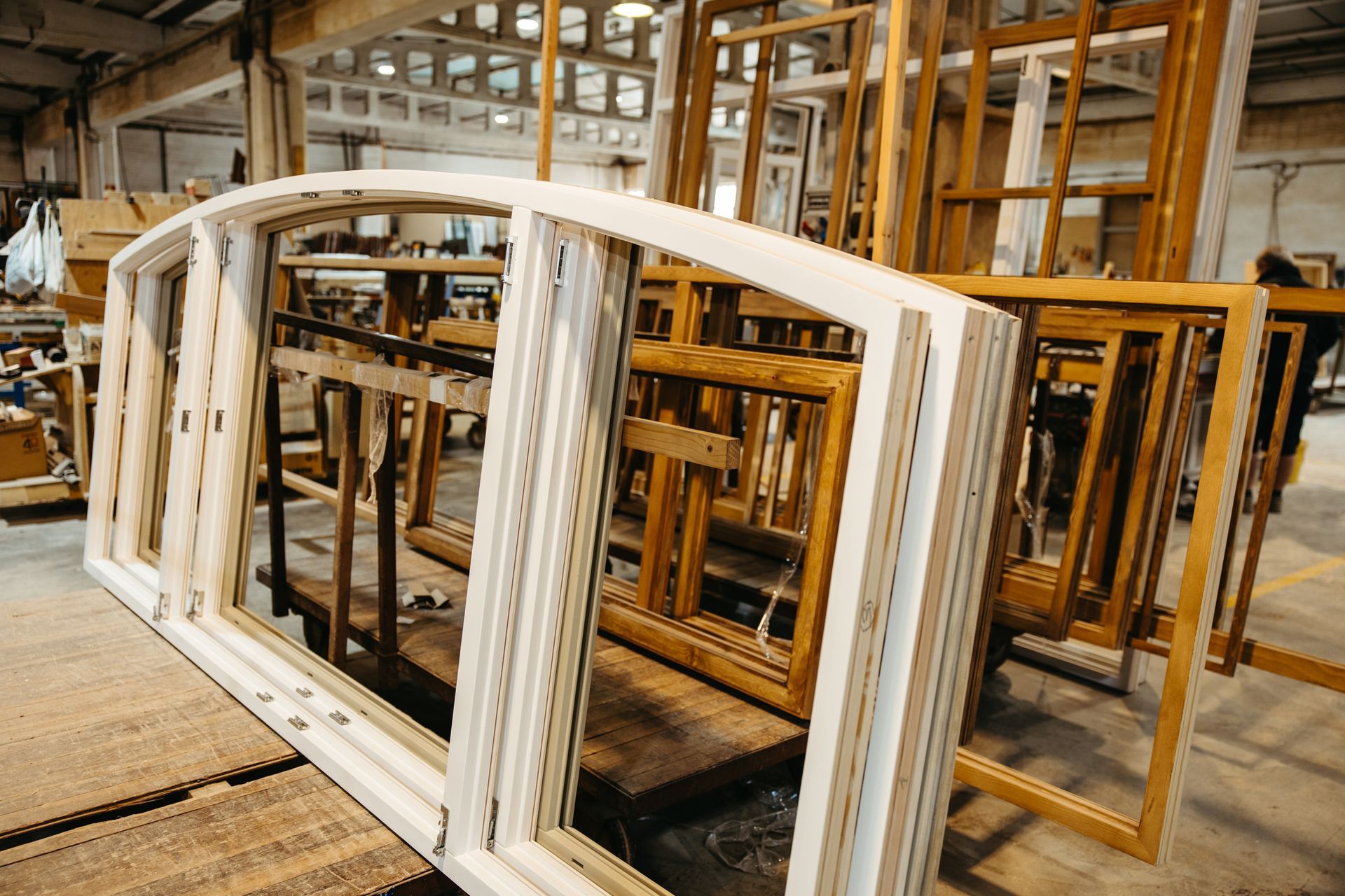 Cadres de fenêtres blancs et en bois empilés dans une usine, lumière naturelle.