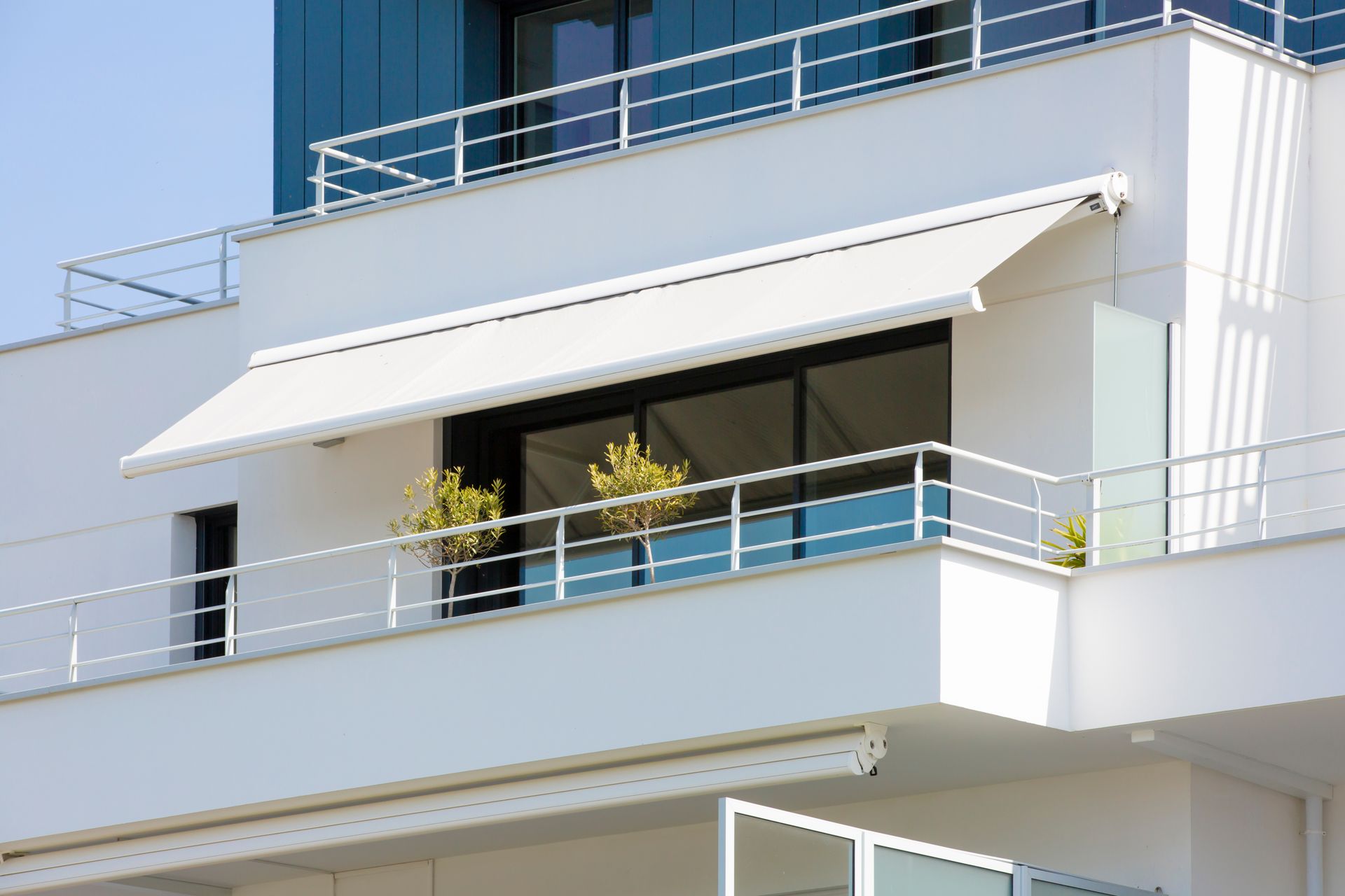 Une fenêtre équipée d’un store extérieur blanc, installée sur un balcon moderne avec des plantes en pot.