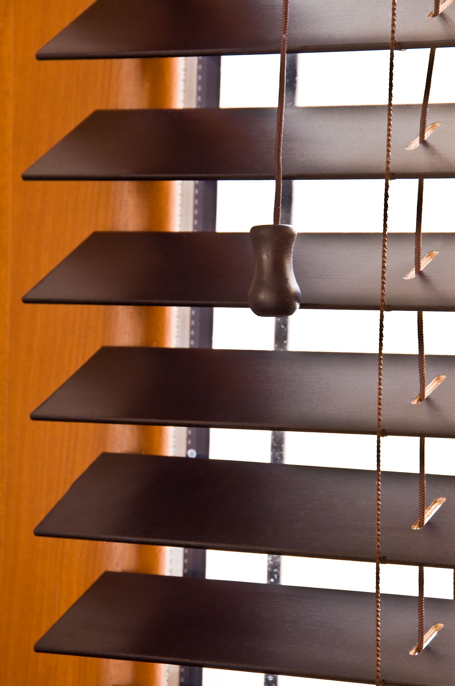 Gros plan sur des stores vénitiens en bois brun, à lamelles inclinées, avec un cordon de tirage et un mur en bois en arrière-plan.