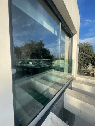 Una persona con camisa gris y pantalones oscuros limpia el escaparate de una tienda con un paño verde.