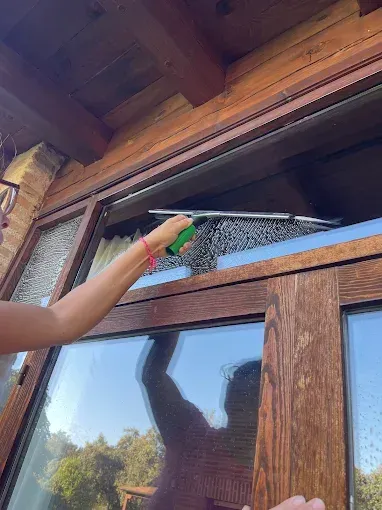 Una persona utiliza una espátula de goma manual para limpiar el cristal superior