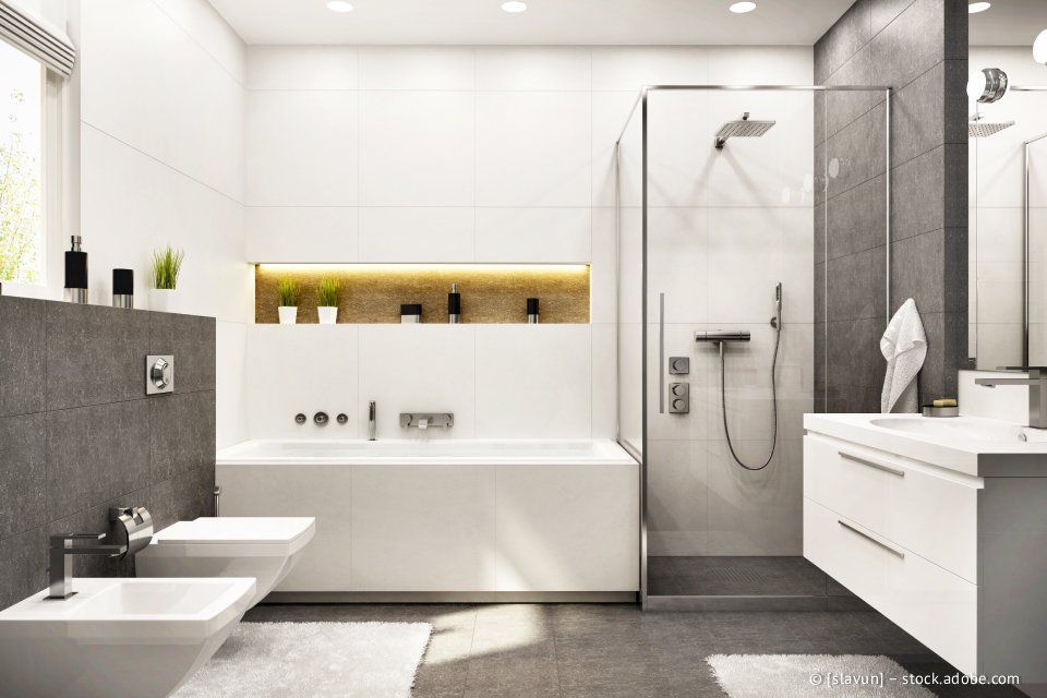 Modernes Badezimmer mit weißen und grauen Fliesen, eingebauter Badewanne, Dusche und schwebendem Waschtisch.