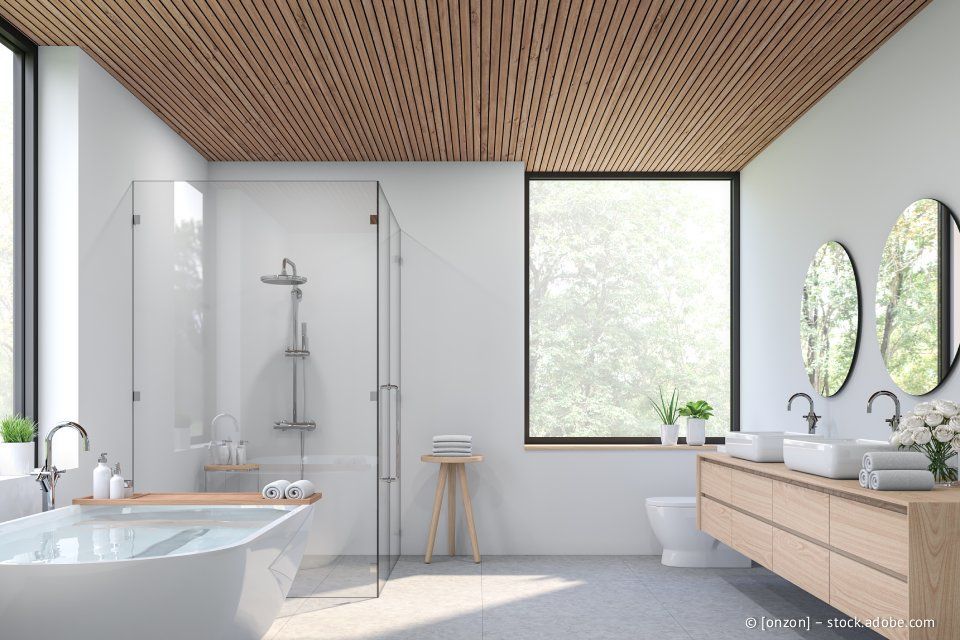 Modernes weißes Badezimmer mit Holzdecke, großen Fenstern, Glasdusche und Waschtisch aus Holz.