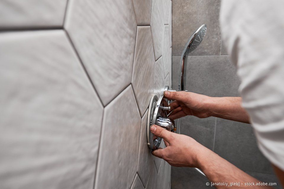 Eine Person montiert eine verchromte Duscharmatur an einer sechseckigen Fliesenwand.