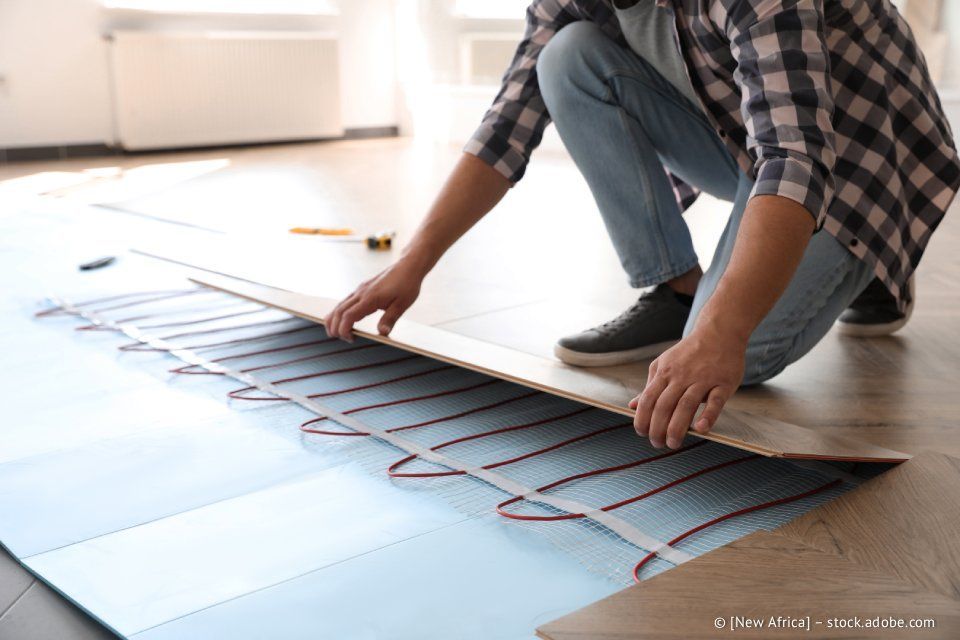 Eine Person verlegt Holzdielen über einer Fußbodenheizung.