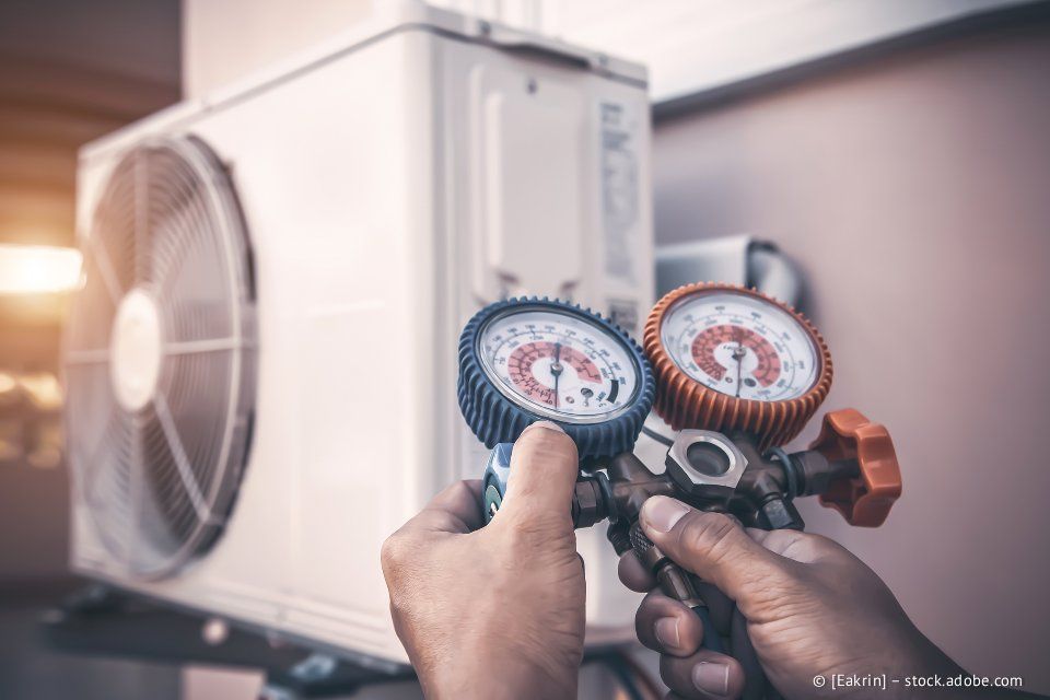 Eine Person überprüft mit Messgeräten eine Außeneinheit einer Klimaanlage.