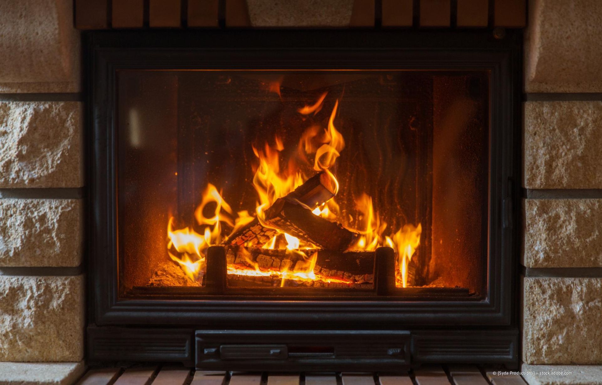 Kamin mit brennenden Holzscheiten, hellen Flammen und gemauerter Umrandung.