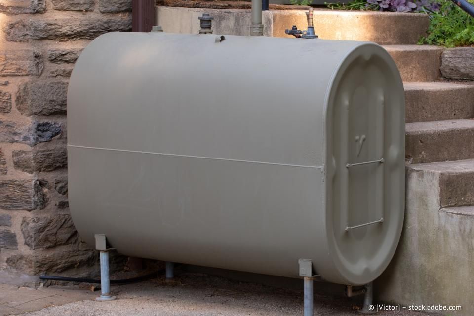 Olivgrüner Öltank, im Freien, in der Nähe von Steinstufen. Der Tank ist zylindrisch und steht auf Metallbeinen.