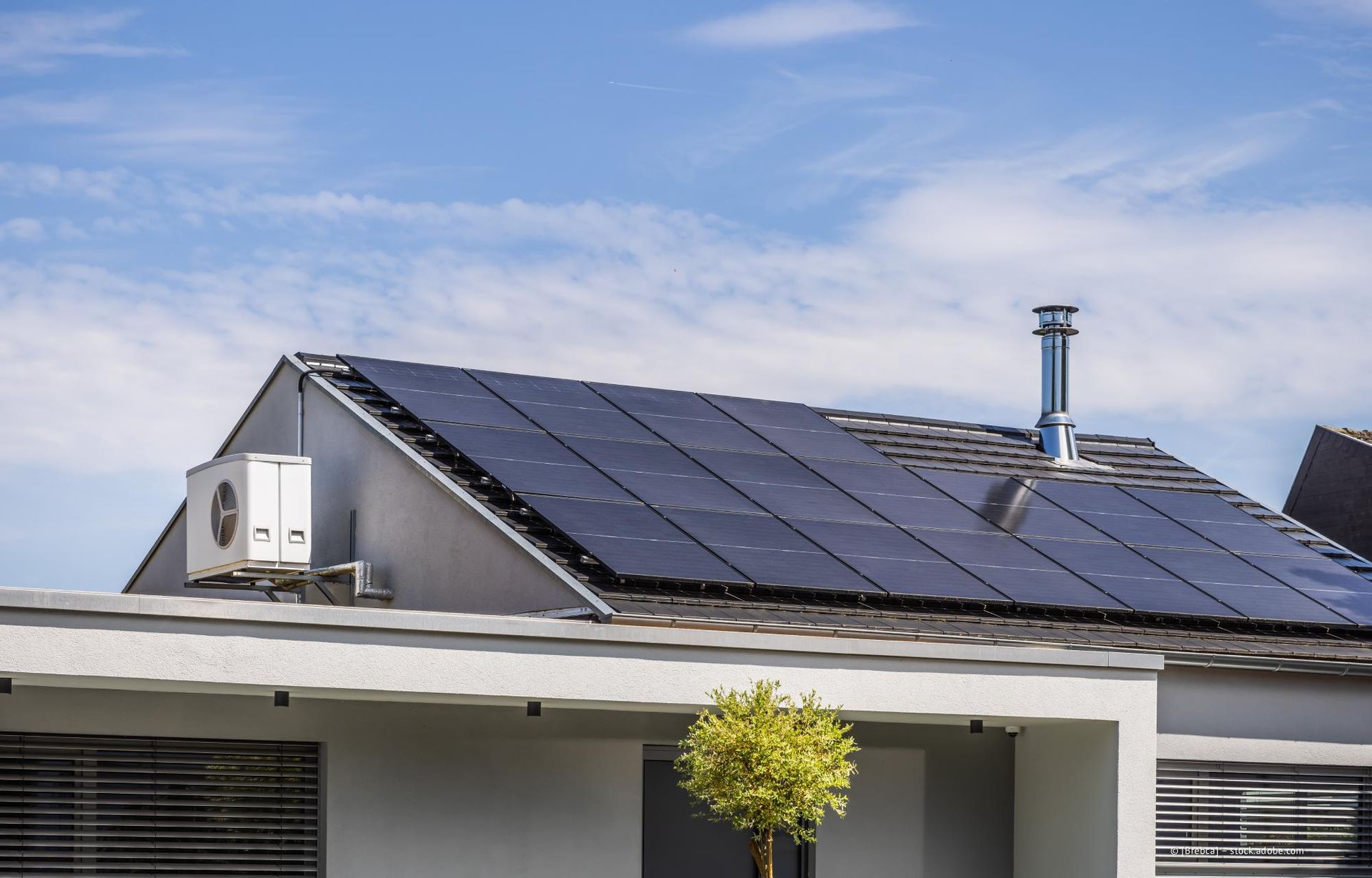 Solarpaneele auf einem Wohnhausdach mit Klimaanlage und Schornstein. Blauer Himmel im Hintergrund.