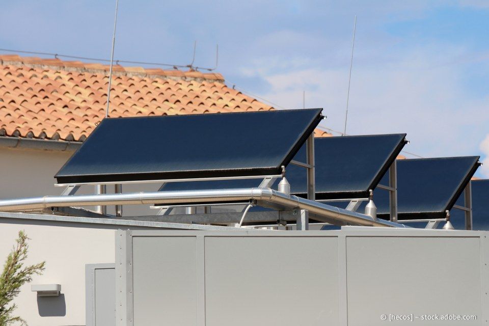 Auf einem Gebäudedach montierte Solarpaneele, zum Himmel geneigt; im Hintergrund blauer Himmel und rotes Ziegeldach.