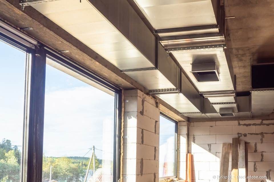 Innenbaustelle mit rechteckigen Lüftungskanälen in der Nähe eines großen Fensters.