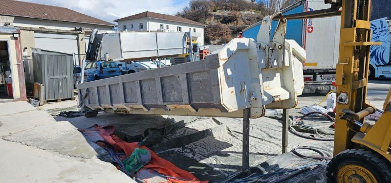Un camion à benne basculante est soulevé par un chariot élévateur dans un parking.