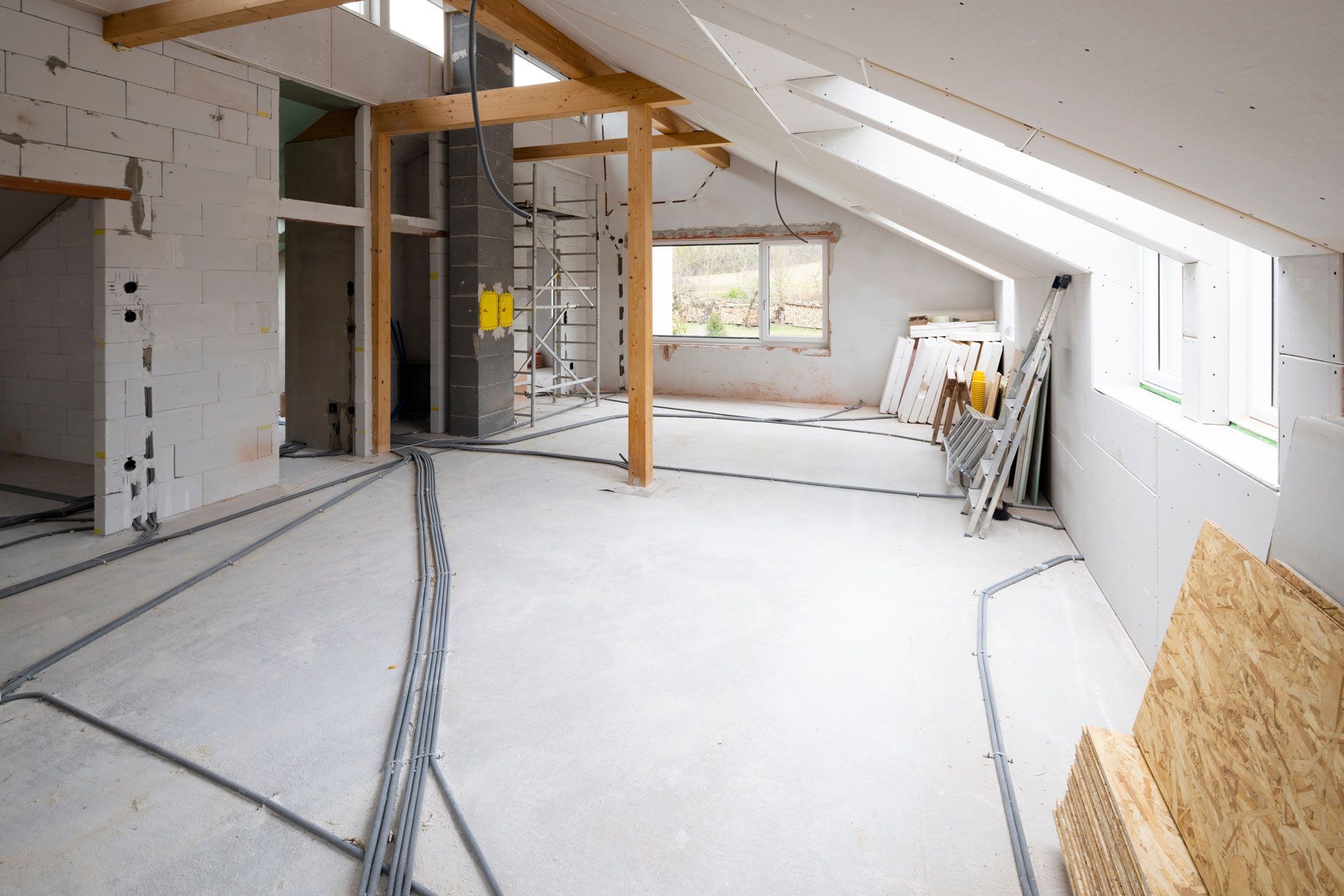 Rénovation intérieure d'une pièce avec poutres apparentes, cloisons sèches et sol en béton.