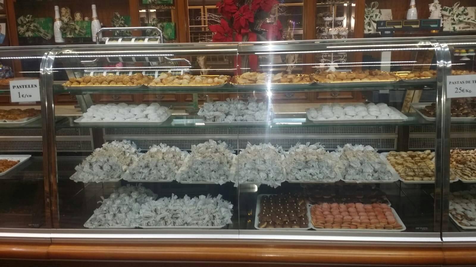 Una vitrina en una panadería repleta de filas de pasteles, galletas y dulces envueltos, distribuidos en varios estantes.