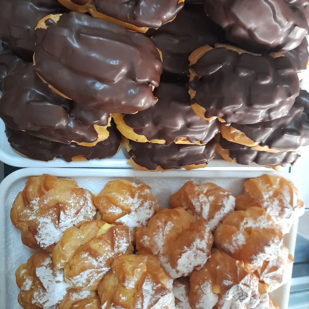 Dos bandejas llenas de profiteroles: una cubierta con glaseado de chocolate negro y la otra espolvoreada con azúcar glas.