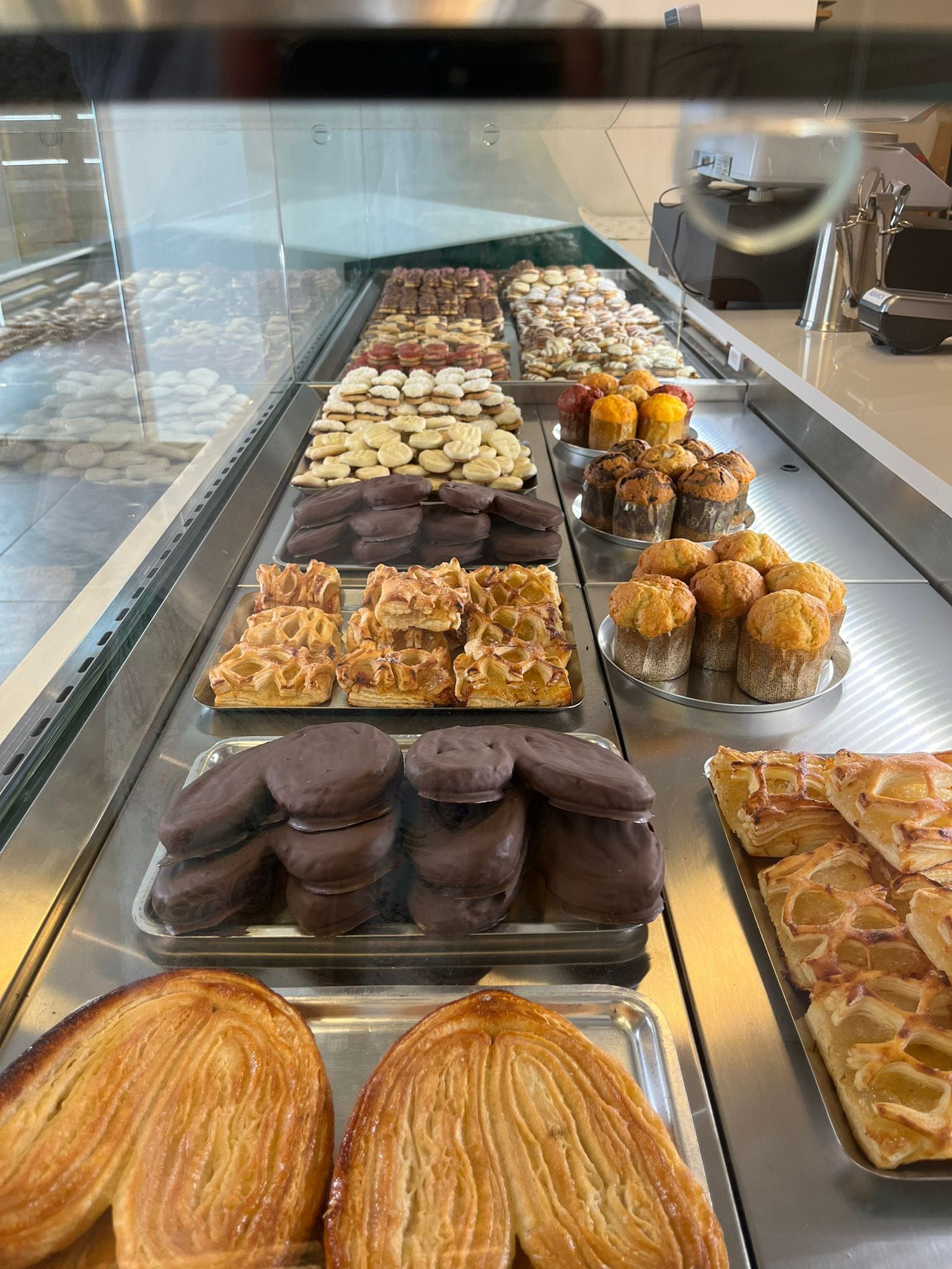 Una variedad de pasteles, galletas y dulces cubiertos de chocolate dispuestos en filas dentro de una vitrina de panadería.
