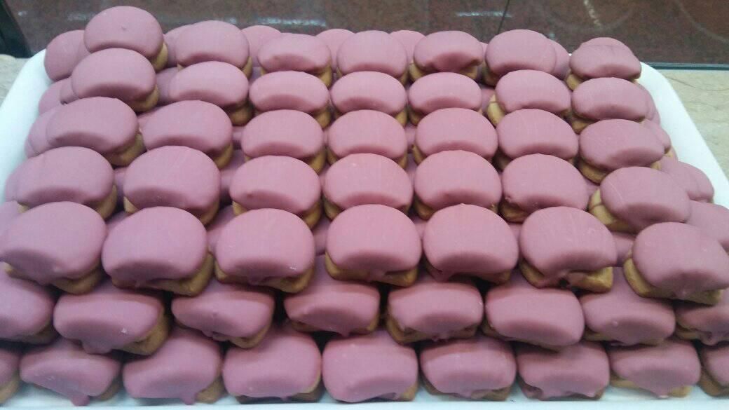 Una bandeja llena de filas de galletas redondas, glaseadas de color rosa claro.