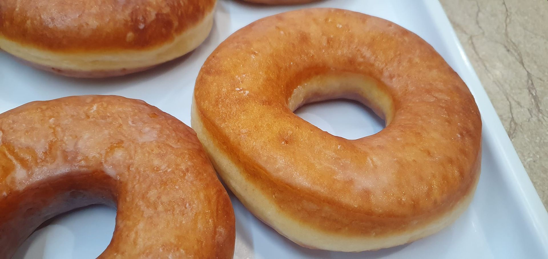 Una bandeja de rosquillas glaseadas de color marrón dorado dispuestas sobre una superficie blanca.
