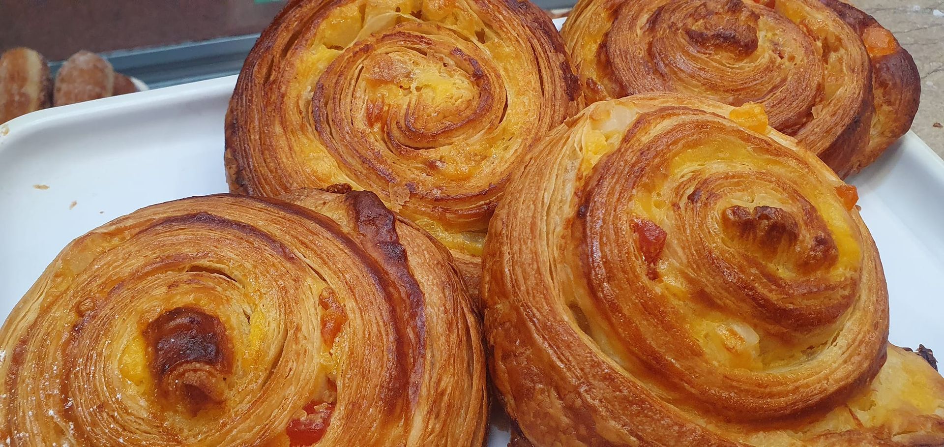 Pasteles dorados con forma de espiral y relleno de crema pastelera visible, dispuestos en una bandeja blanca.