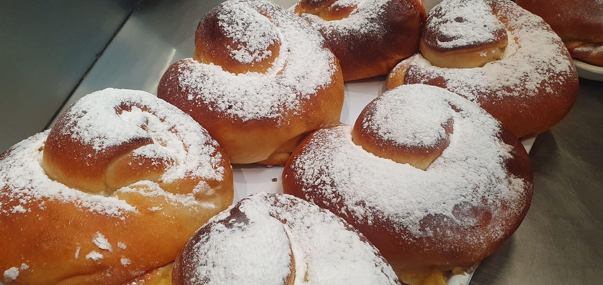 Varios panecillos brioche recién horneados, dorados y espolvoreados con azúcar glas, dispuestos en una bandeja metálica.